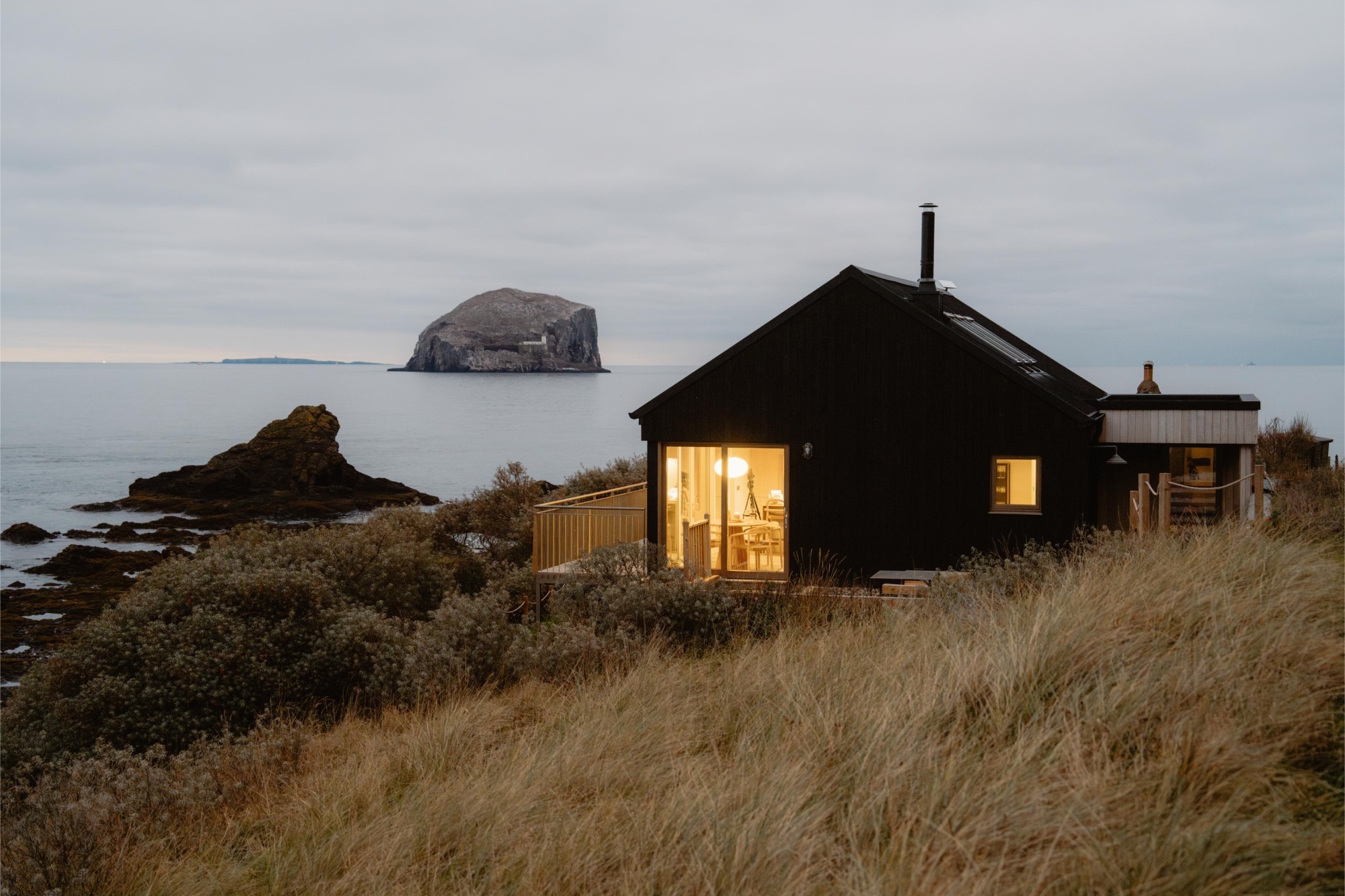 A black timber cabin on a wild coastline at dusk